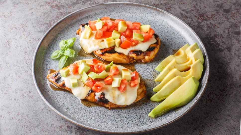 Delicious California Grilled chicken breast with mozzarella cheese, avocado and tomatoes close-up in a plate on the table. horizontal