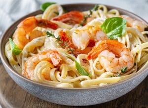 Pasta with shrimps and herbs in a plate on the table, close-up