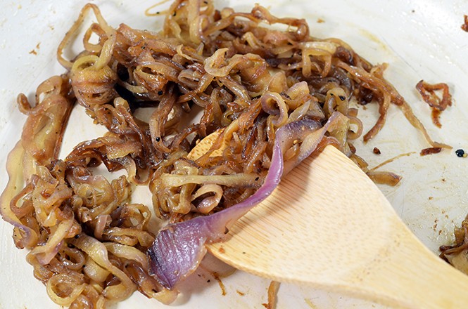 Wooden spatula stirring caramelized onions in saute pan