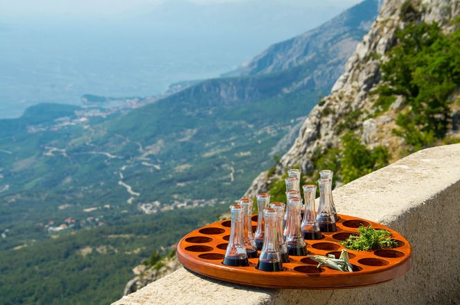 Pladanj s bocama vina i persinom ispred brezuljaka i stijena Biokova i Makarske rivijere 