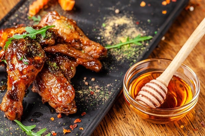 1292748448 The concept of Indian cuisine. Baked chicken wings and legs in honey mustard sauce. Serving dishes in the restaurant on a black plate. Indian spices on a wooden table. background image.