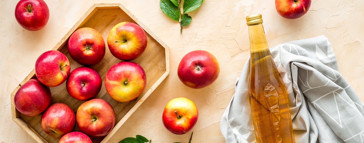 1814741072 Apple cider vinegar in glass bottle and wooden tray with red apples