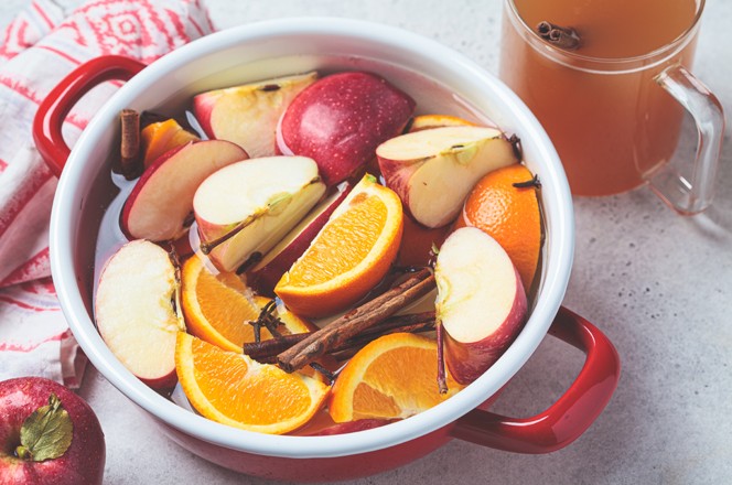 Cooking homemade hot cider from apples and oranges with spices in a red saucepan. Autumn or winter warming drink.