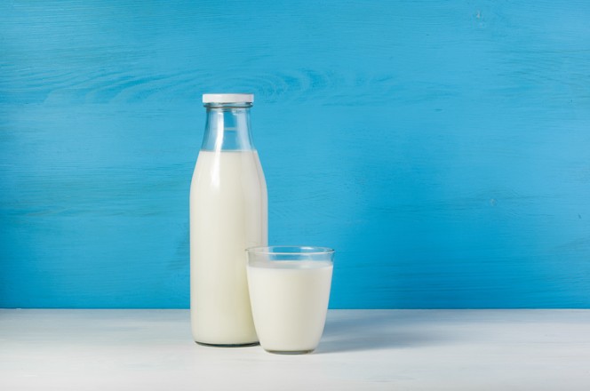 A bottle of rustic milk and glass of milk on a white table on a blue background, tasty, nutritious and healthy dairy products