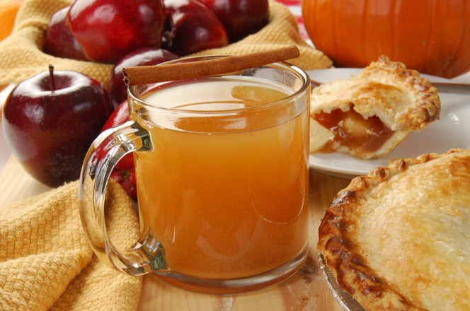A cup of hot apple cider by an apple pie