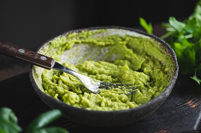 1946397976 Umak od zgnjecenog avokada u zdjelici na tamnoj podlozi. Zdrav veganski umak od avokada.