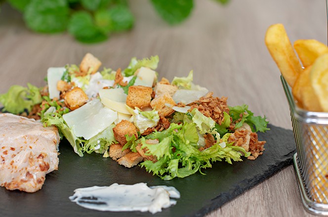 2028954935 Endivija salata s fileom pecene pilece prsa, krutonima, plo kama Manchego sira i hrskavim lukom na crnom kamenoj podlozi, uz pomfrit.