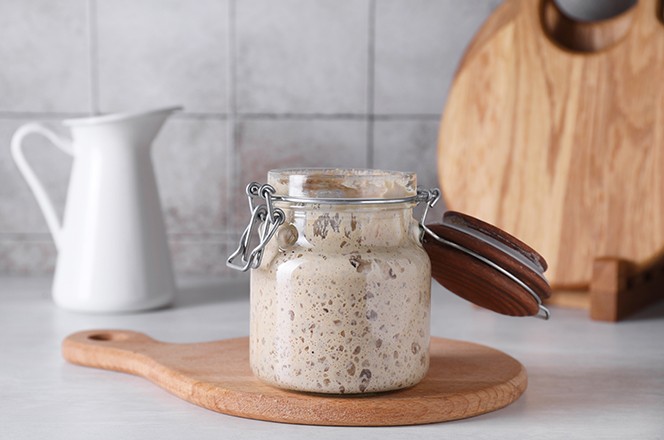 2456002435 Kvas (sourdough starter) u staklenoj staklenci na svijetlom stolu.