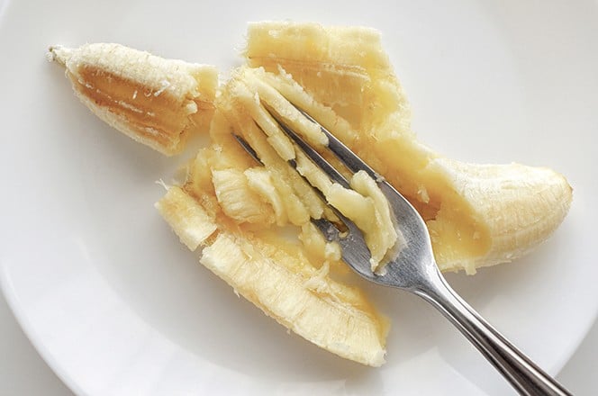 2465595931 Zrela banana koja se gnjeci vilicom na bijelom tanjuru. Pire od banane na tanjuru. Koncept zdrave i dijetalne prehrane.