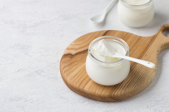 2318066589 Prirodni domaci jogurt u staklenoj teglici na drvenoj dasci, na svijetlosivoj podlozi.