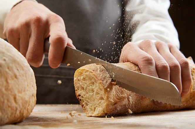 2340557811 Izbliza prikazan mu karac koji re e svje i hrskavi baguette kuhinjskim no em na drvenom stolu.
