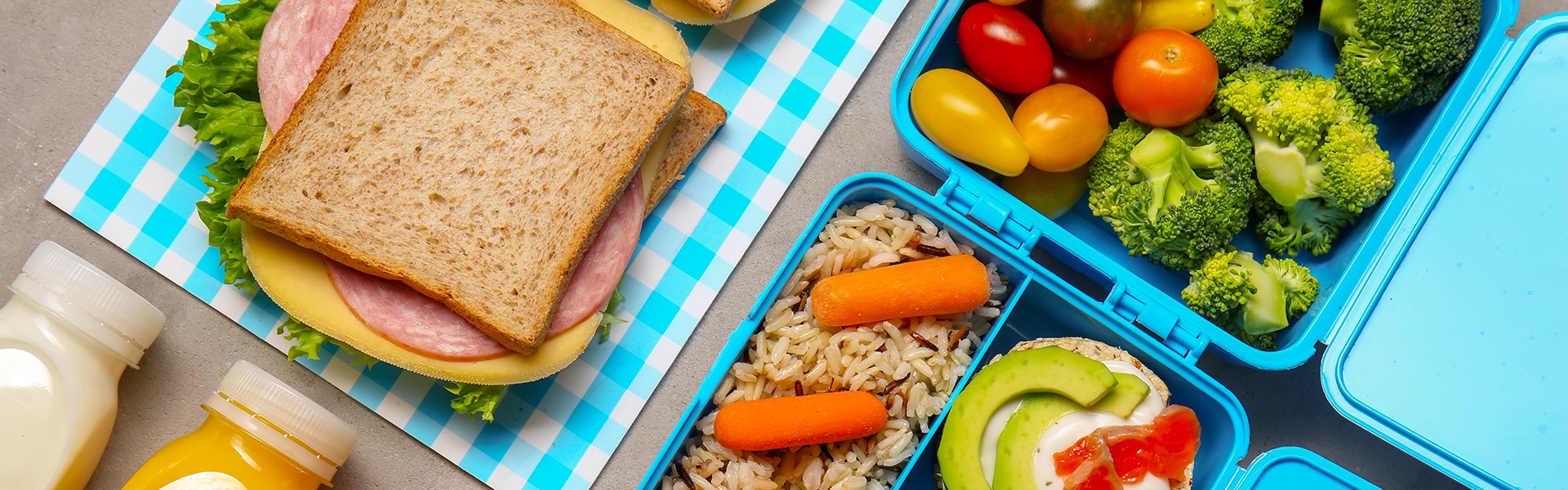Lunch boxes with tasty food and bottles of drinks for kid on grey background
