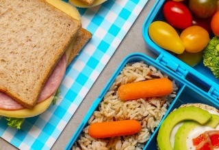 Lunch boxes with tasty food and bottles of drinks for kid on grey background