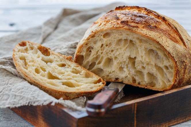 Cut loaf of artisanal wheat bread in a wooden box on a white table, selective focus.
