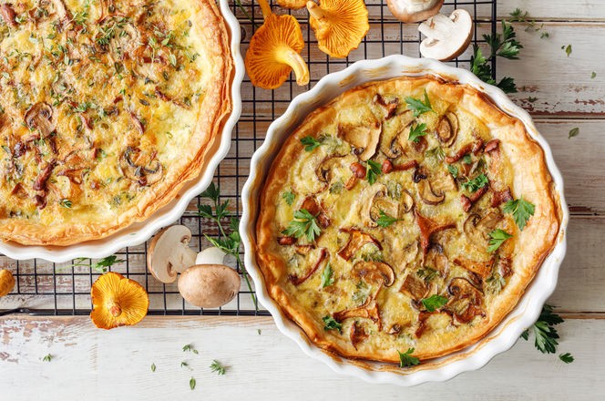 Mushroom quiche with addition chanterelle mushrooms and brown mushrooms on a wooden white table, close up, top view