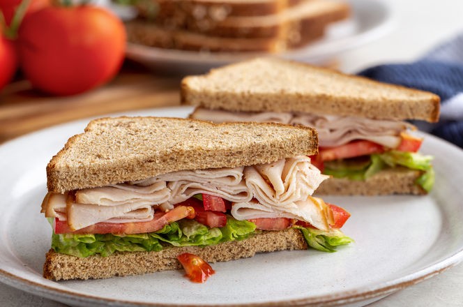 Healthy sandwich with turkey, tomato and lettuce on whole wheat bread on a white plate