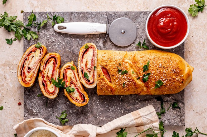 Stromboli pizza sliced on a blue marble served with tomato sauce and parmesan cheese sprinkled with fresh parsley, top view