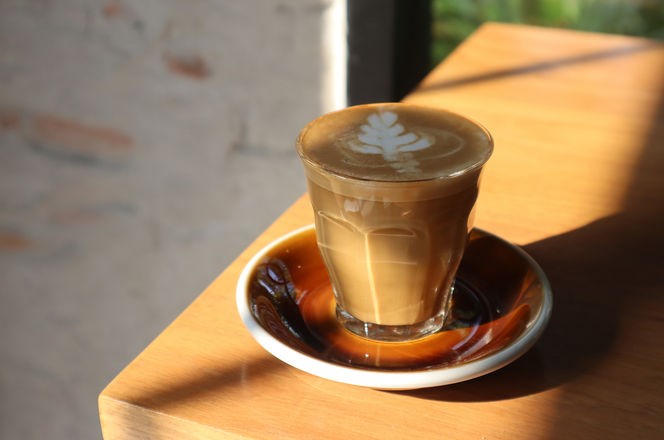 Flat white coffee in crystal glass on wooden table. Flat white is less frothy than traditional cappuccino, has less milk than latte. 