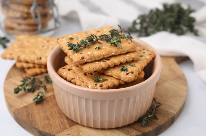 Cereal crackers with flax, sesame seeds and thyme in bowl on light table, closeup