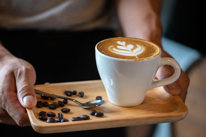 White ceramic cups of cappuccino with latte art Barista make coffee by pouring spills hot milk cream on black coffee. Barista serve holding cup of hot latte and coffee beans on wooden table cafe shop