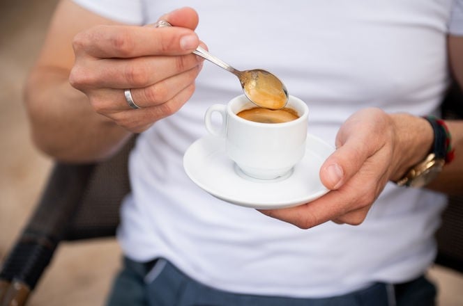 Close-up of a man stirring a cup of espresso with a spoon, creating a cozy and relaxing moment. Perfect for depicting coffee culture and mornings.