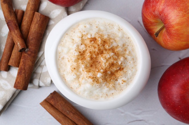 Delicious rice pudding with apples and cinnamon sticks on white textured table, flat lay