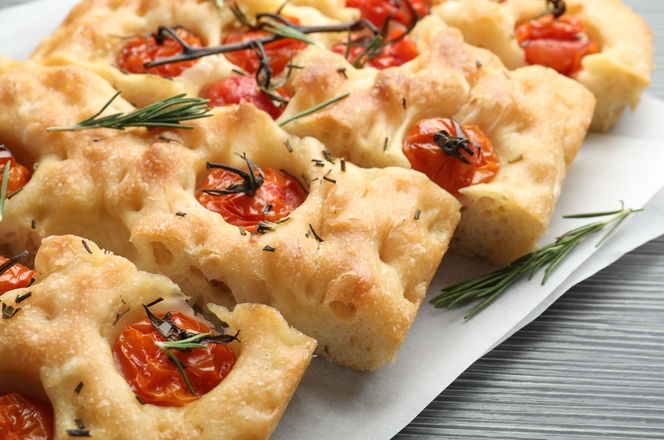 Cut delicious focaccia with tomatoes and spices on table, closeup