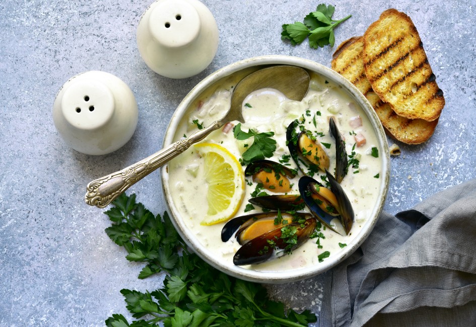 Chowder - delicious fish soup with mussels in a bowl on light grey slate, stone or concrete background. Top view with copy space.